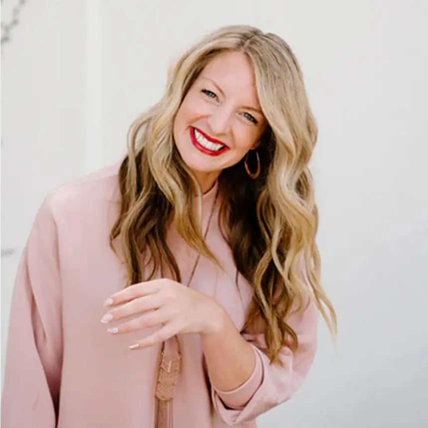 A photo of Chelsea, a white woman with long blonde hair, blue eyes and red lipstick. She is wearing a pale pink blouse and smiling broadly at the camera