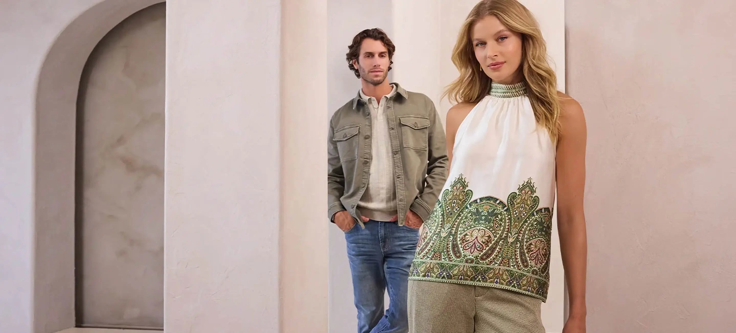 Man and woman standing side by side in a neutral setting, wearing stylish outfits.